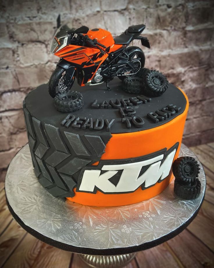 an orange and black birthday cake with a motorcycle on the top, sitting on a silver platter