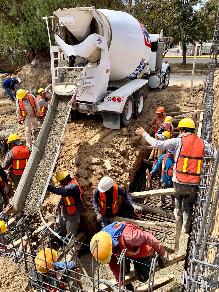 construction workers working on the side of a road with a cement truck in the background