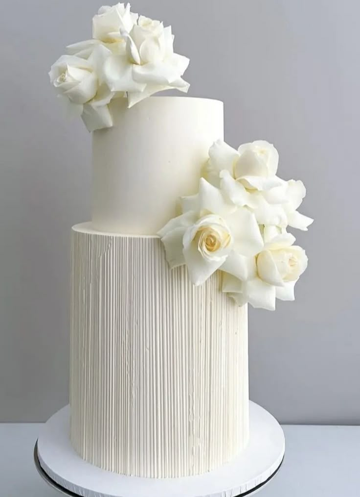 a three tiered white cake with flowers on the top and bottom, sitting on a plate