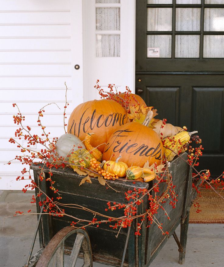 a wagon filled with pumpkins sitting in front of a door and welcome sign on it