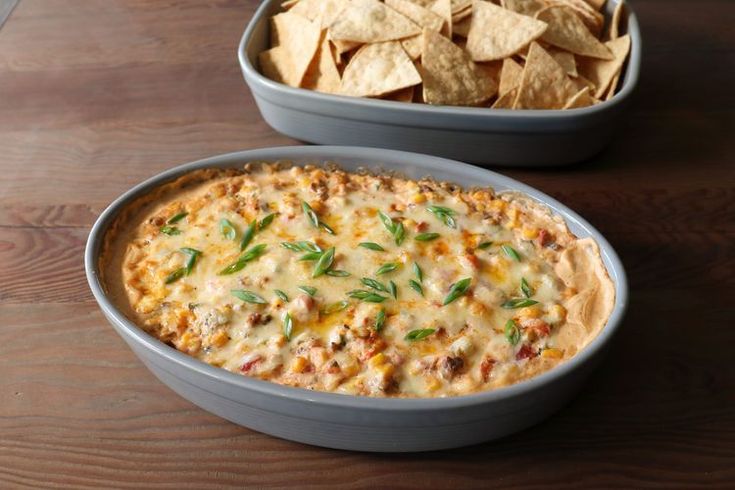 two bowls filled with dip and tortilla chips next to each other on a wooden table