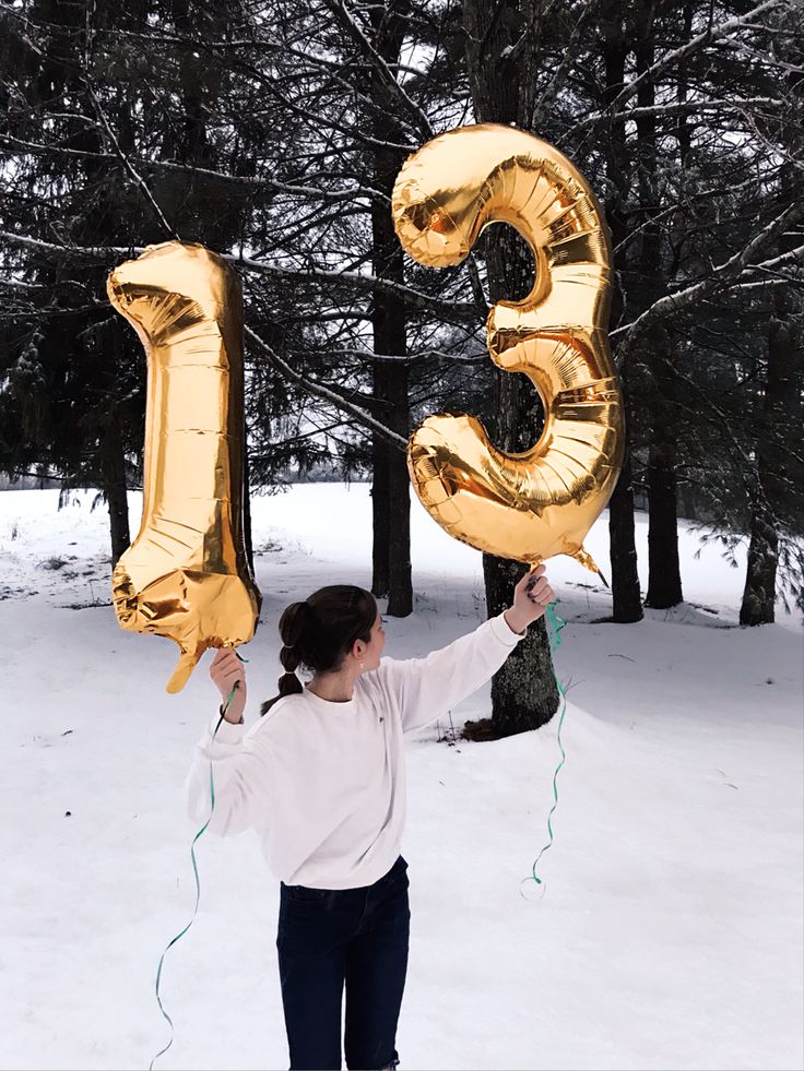 a woman holding two large gold balloons in the shape of numbers 3 and 5, while standing in the snow