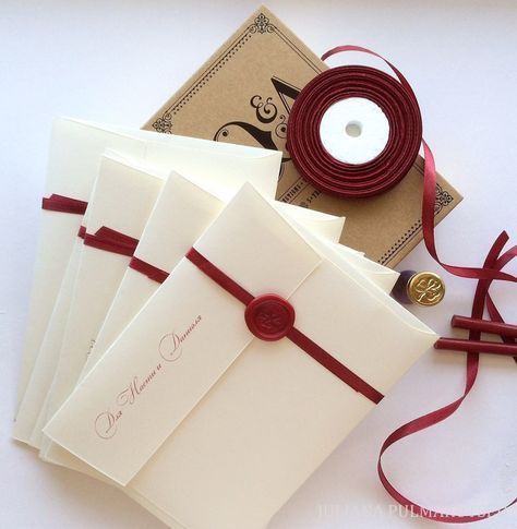 four cards with red ribbon and button on them, sitting next to a white candle