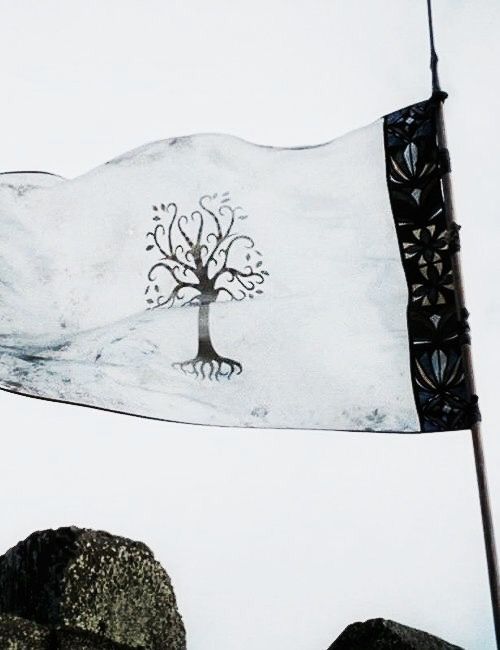 a white flag with a tree on it flying in the sky over rocks and trees