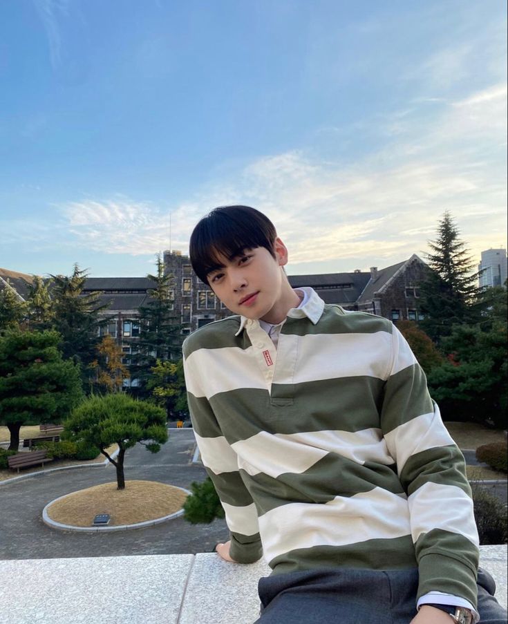 a young man sitting on top of a building next to a tree filled park with buildings in the background