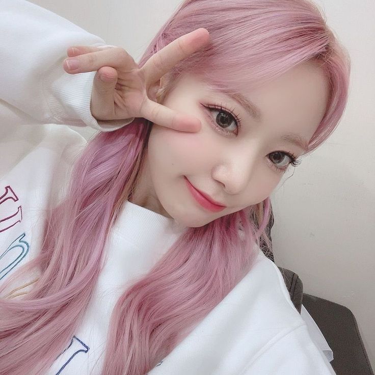 a girl with long pink hair is making the v sign while wearing a white sweatshirt