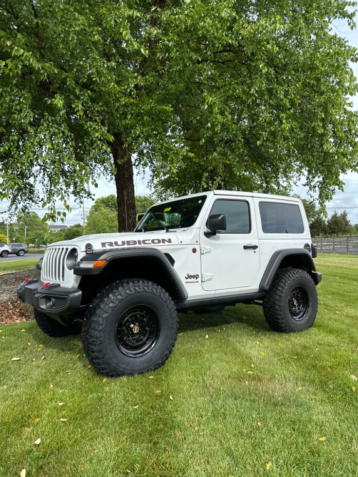 a white jeep parked under a tree in the grass