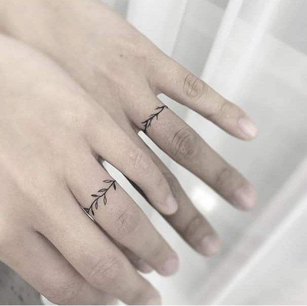 two fingers with small tattoos on them, one has an arrow and the other has a leaf