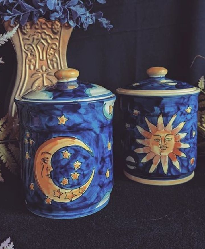 two ceramic containers with sun and moon designs on them, next to a vase filled with flowers