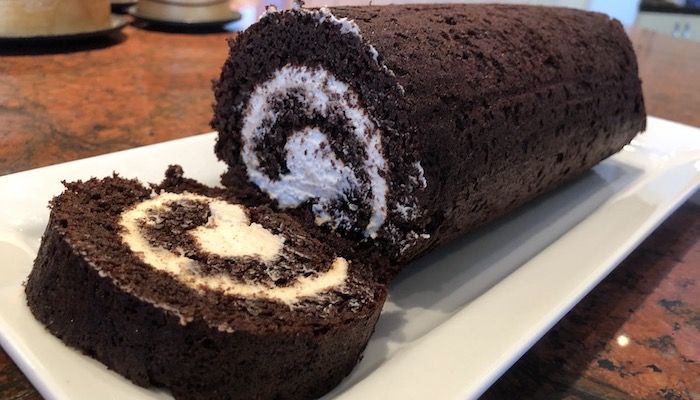 there is a chocolate roll with white frosting on the plate and it has been cut in half