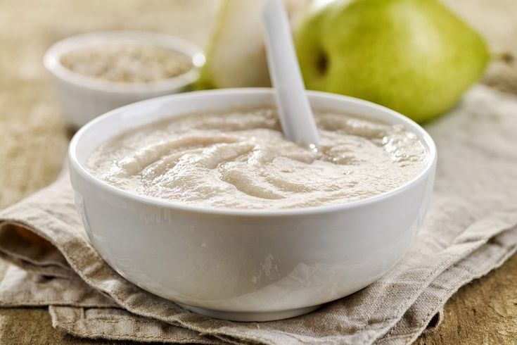 a bowl of oatmeal next to two green apples on a cloth with spoons