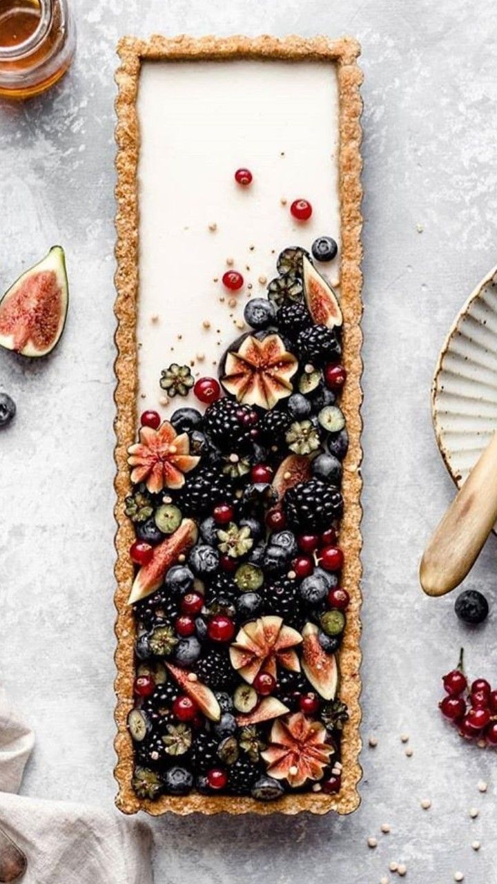 a tart with fruit and berries on it, next to other food items such as figurines