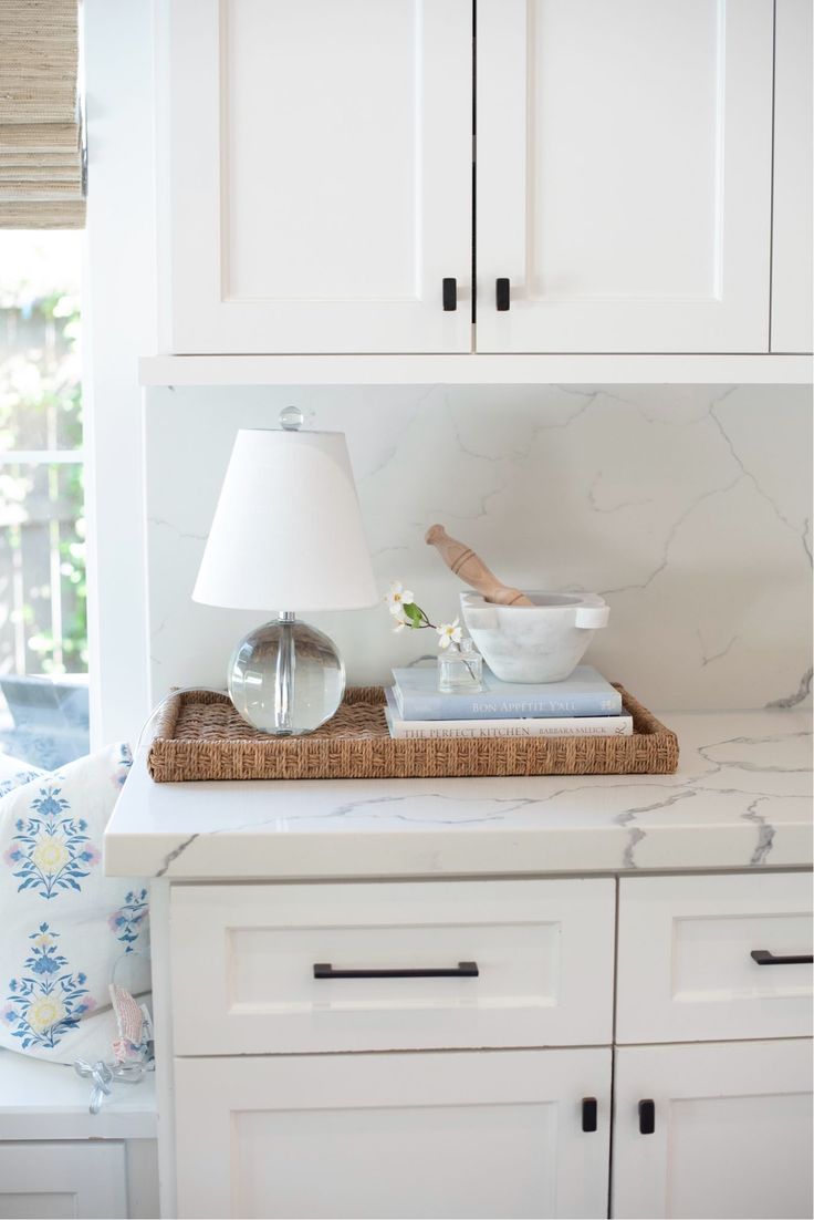 a kitchen with white cabinets and marble counter tops, including a basket on the island