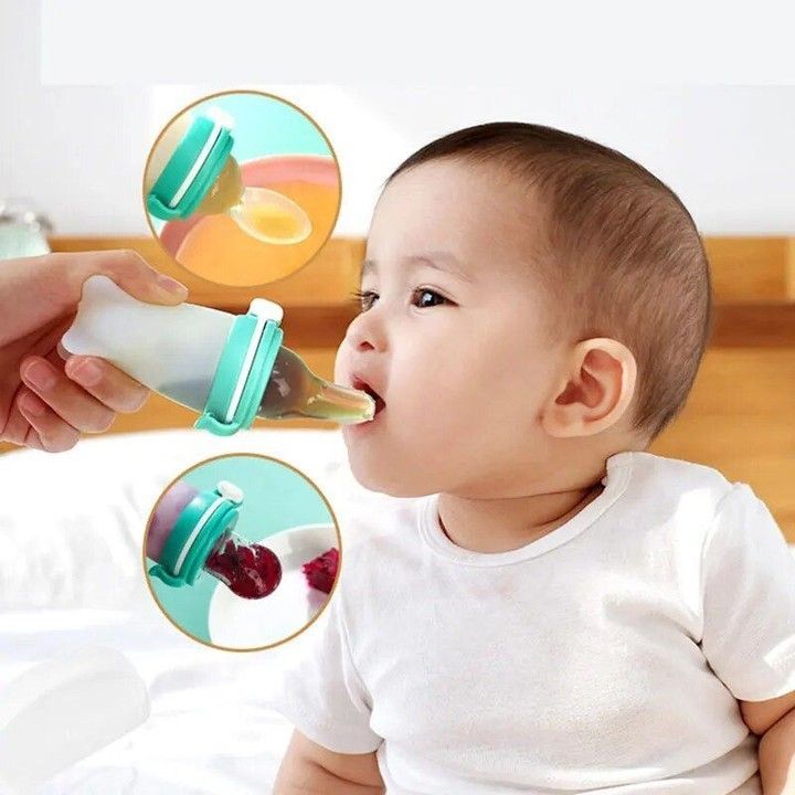 a baby sitting on a bed drinking from a bottle with an adult hand holding it