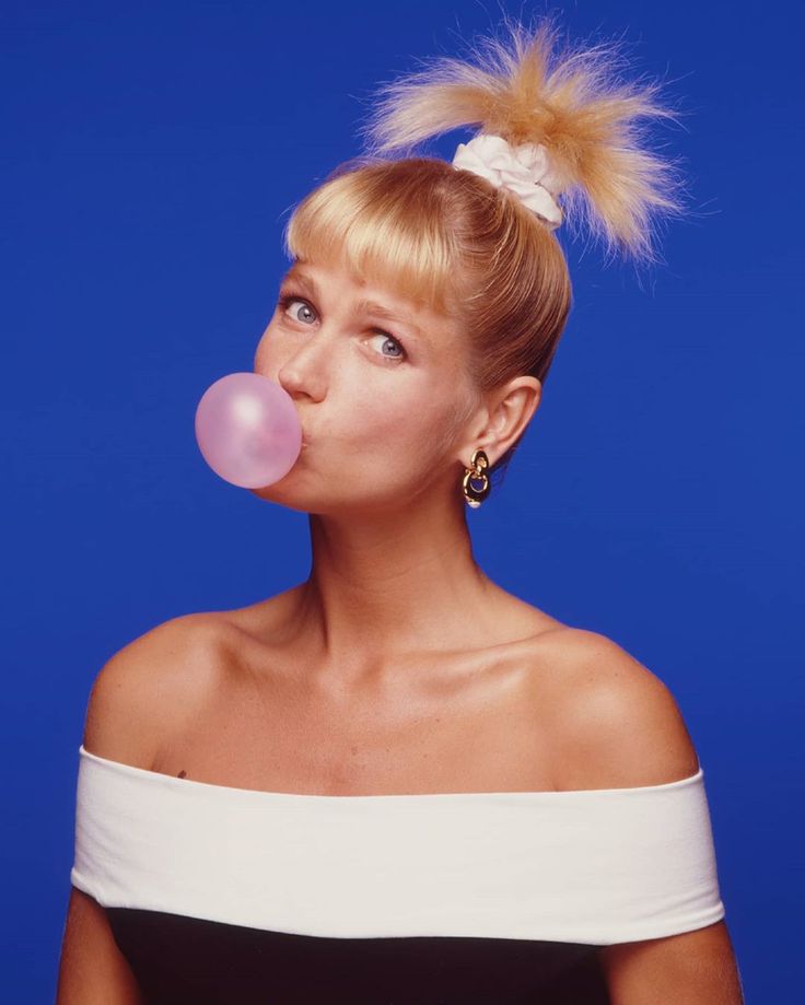 a woman blowing bubbles with her hair in a bun on top of her head, against a blue background