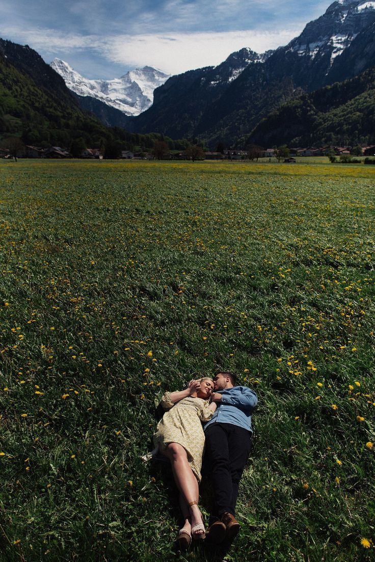 a man and woman laying on the ground in a field with mountains in the background