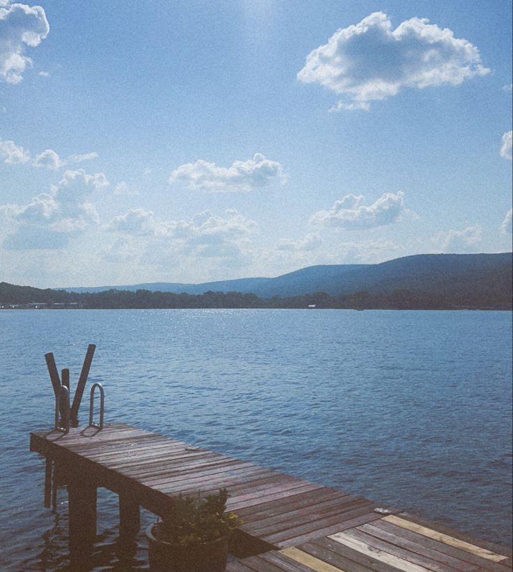 a wooden dock sitting on top of a lake under a blue sky with white clouds