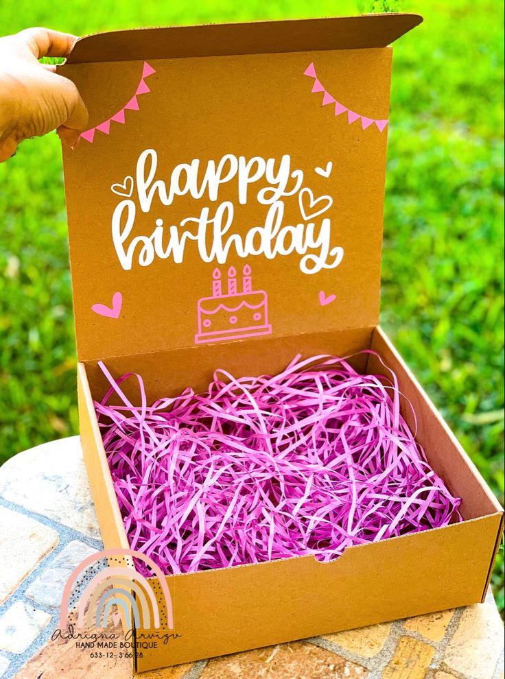 someone is holding up a birthday card in a box with purple shredded paper on it