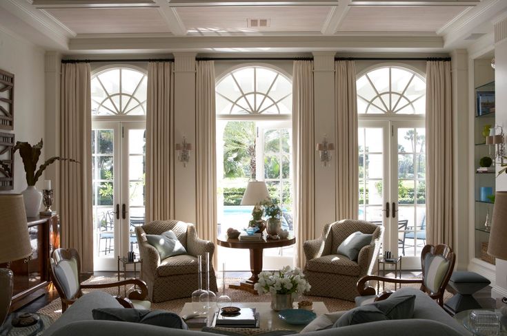 a living room filled with lots of furniture next to two large windows covered in curtains