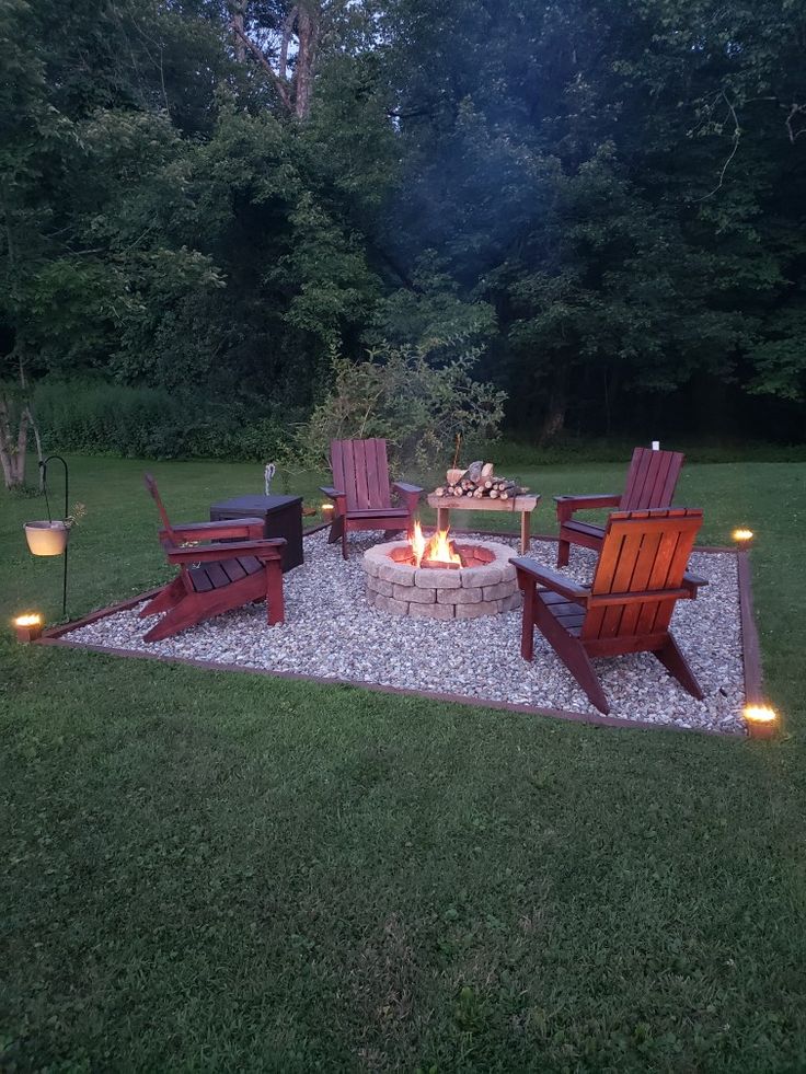 a fire pit surrounded by chairs and lights in the middle of a grassy area with lots of trees