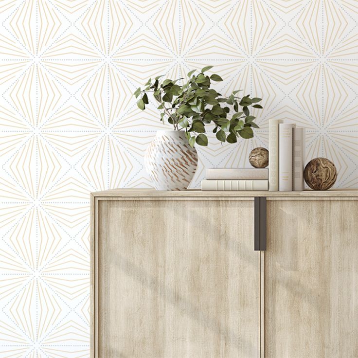 a wooden cabinet sitting next to a wall with a plant on top of it in front of a patterned wallpaper