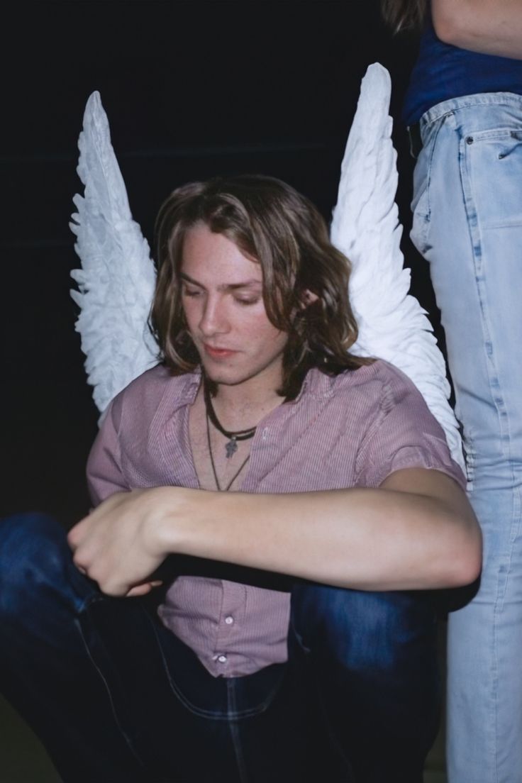 a young man sitting on the ground with angel wings