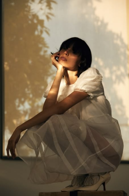 a woman sitting on top of a wooden table next to a shadow filled wall and tree