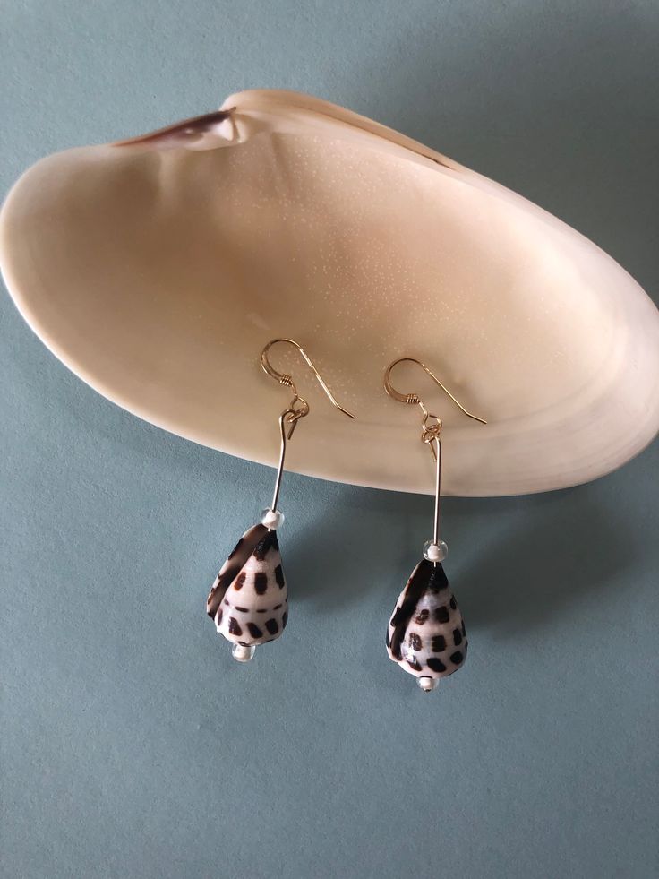 These pieces are one of a kind, made with natural Hebrew Cone seashells. Each shell is unique and will not be identical to each other. Paired with the shells are clear glass beads. Please note that due to the inherent nature of seashells, minor imperfections may be present. The ear wire component is 14k gold filled, perfect for everyday use that will not tarnish.  Please feel free to message me if you have any questions! Cone Shell Jewelry, Unique Handmade Shell Earrings, Handmade Silver Shell For Beach, Handmade Silver Shell Drop Earrings, Unique Silver Shell Necklace For Beach, Mother Of Pearl Shell With Pearl Drop, Silver Shell Earrings For Beach, Nickel-free Shell Dangle Earrings, Beach Earrings Made Of Mother Of Pearl