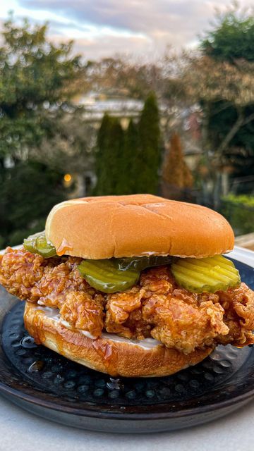 a chicken sandwich with pickles on a black plate