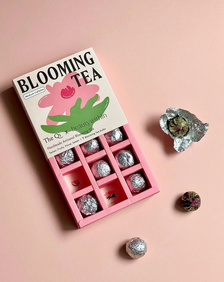 a pink box filled with chocolates next to two pieces of silver foil on top of a pink surface