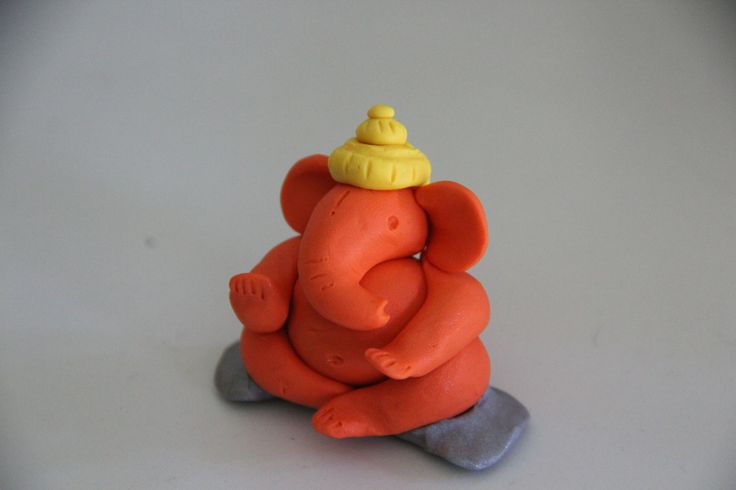 an elephant figurine with a yellow hat on its head sitting on a gray surface