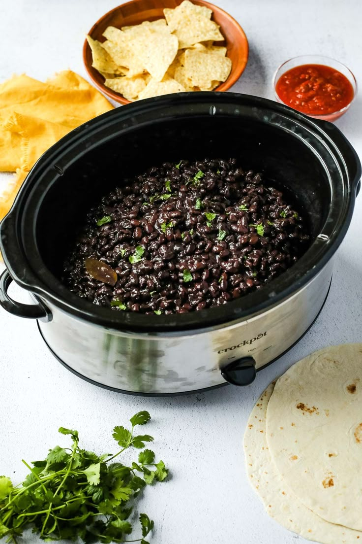 a crock pot filled with black beans and tortilla chips next to salsa