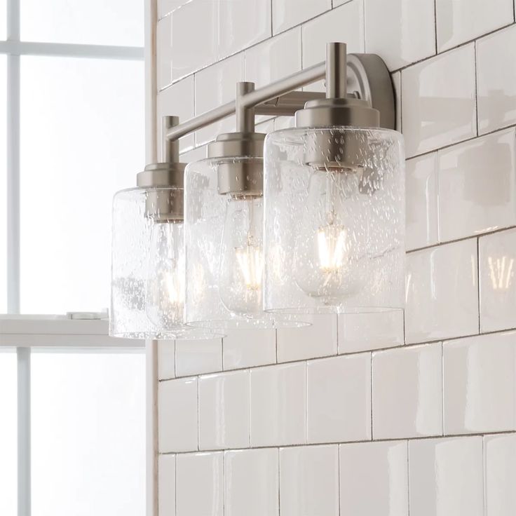 a bathroom light with three lights on it and white tile wall behind the light fixture