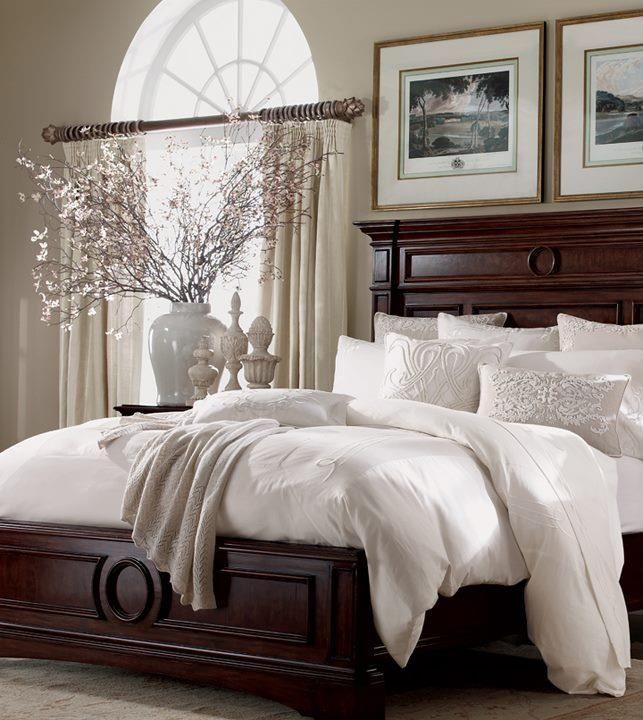 a bed with white comforters and pillows in a living room next to a window