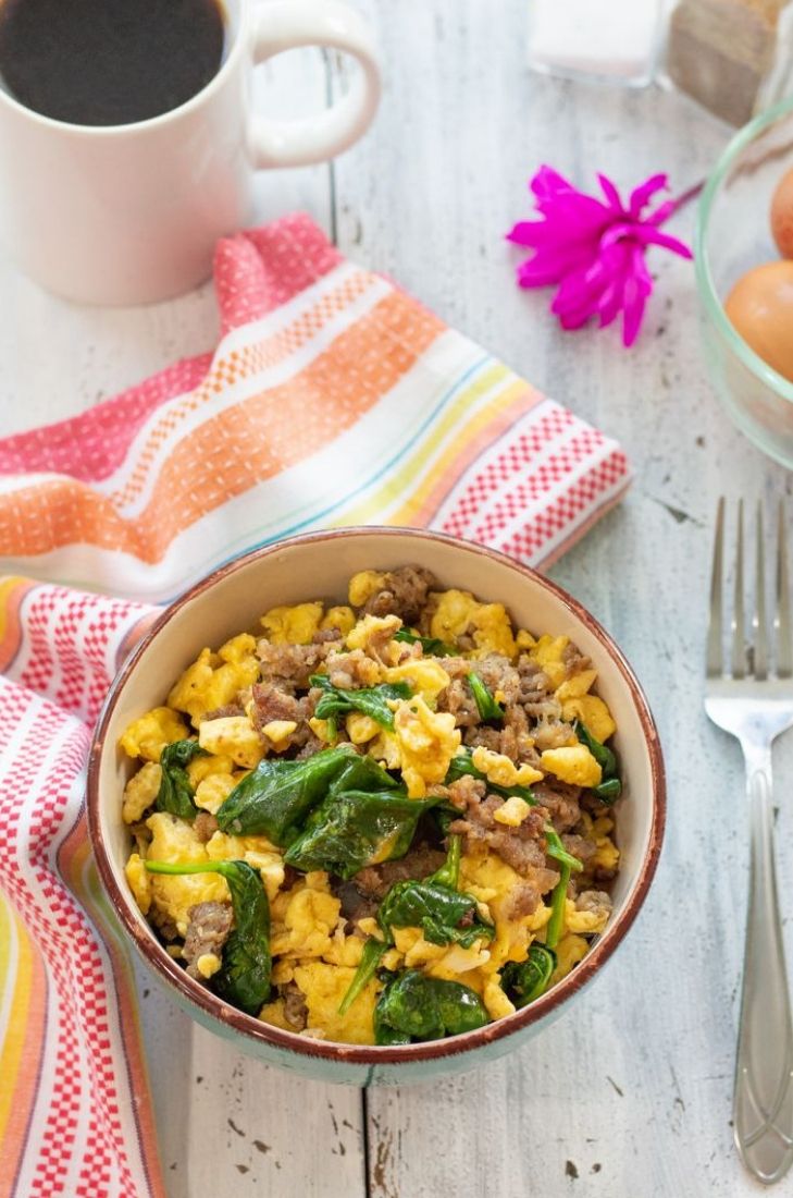 a bowl filled with eggs and spinach next to a cup of coffee on a table