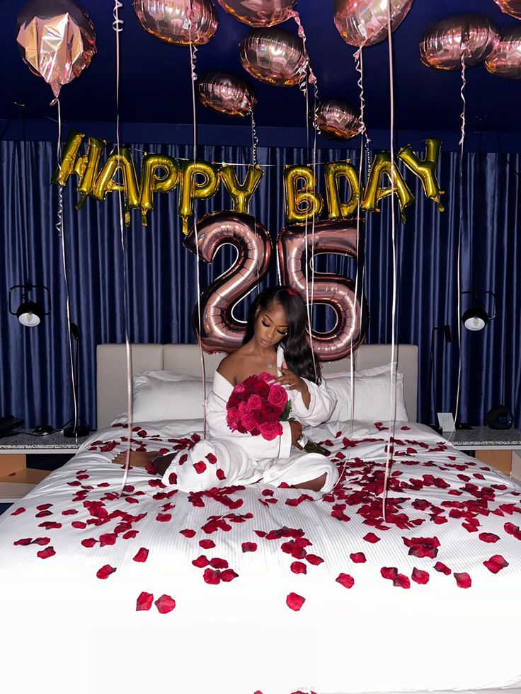 a woman sitting on top of a bed in front of balloons and streamers that say happy birthday