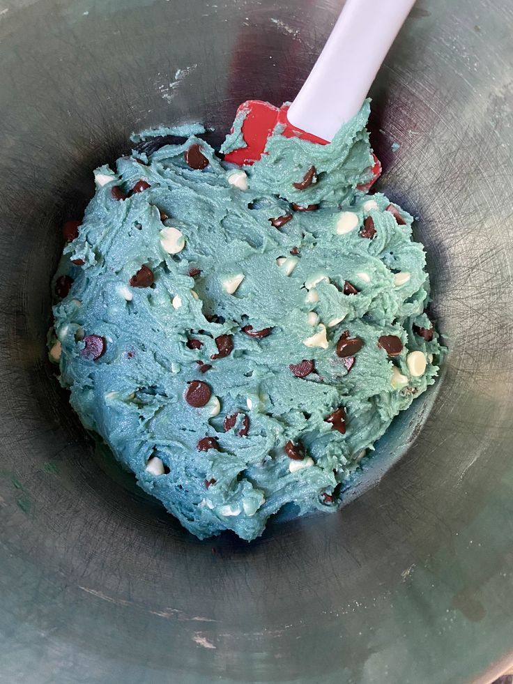 a mixing bowl filled with blue and green frosted cake batter next to a red spatula