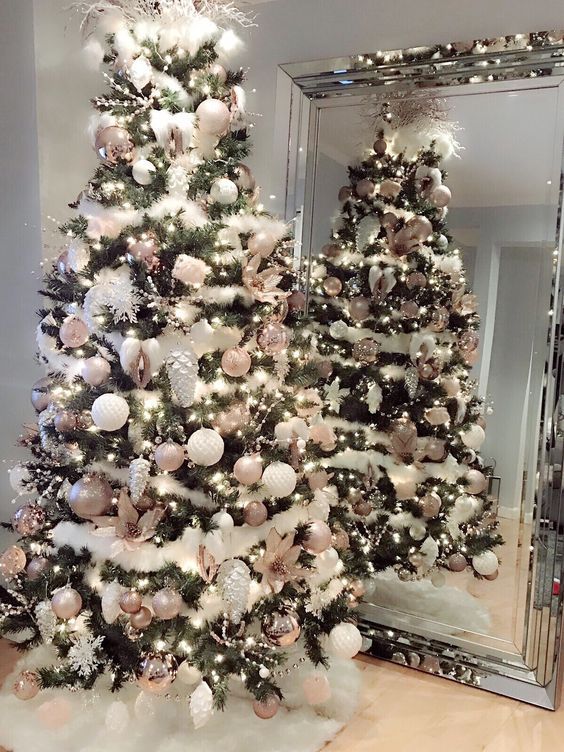 a white christmas tree with pink and silver ornaments in front of a large mirror on the floor