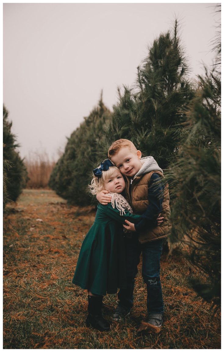 two children hugging each other in the middle of a christmas tree farm with lots of trees