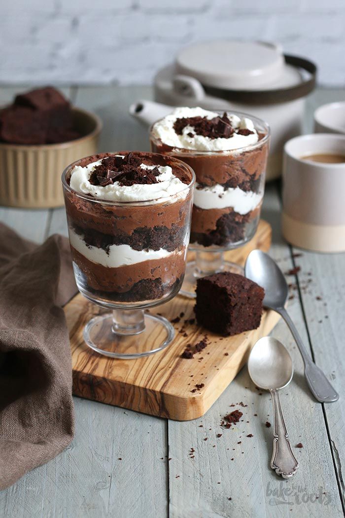 two desserts are sitting on a cutting board with spoons next to the cups