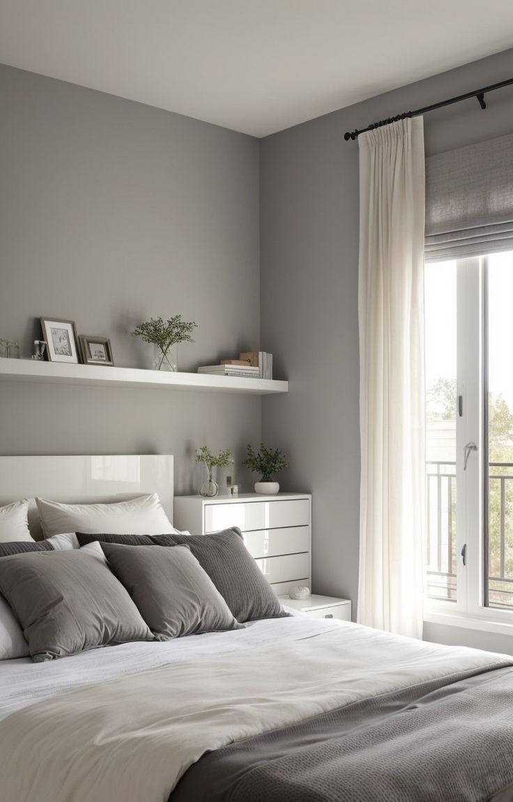 a white bed sitting next to a window with curtains on the windowsill and shelves above it