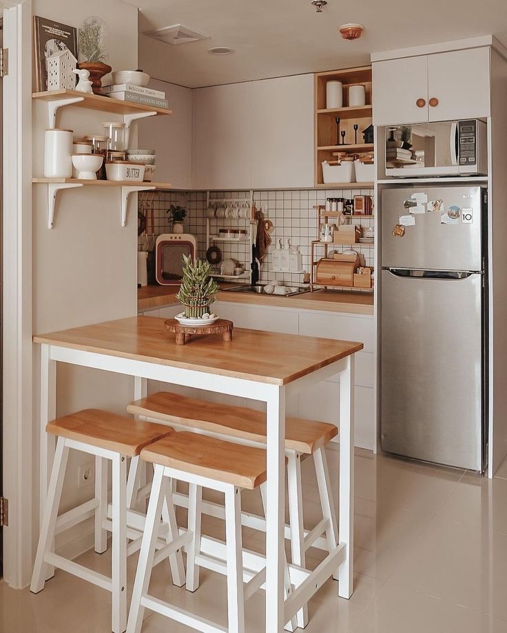 a kitchen with a table and stools next to a refrigerator in the corner,