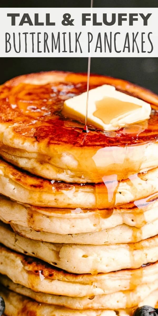 a stack of pancakes with butter on top and blueberries around the edges, in front of a black background