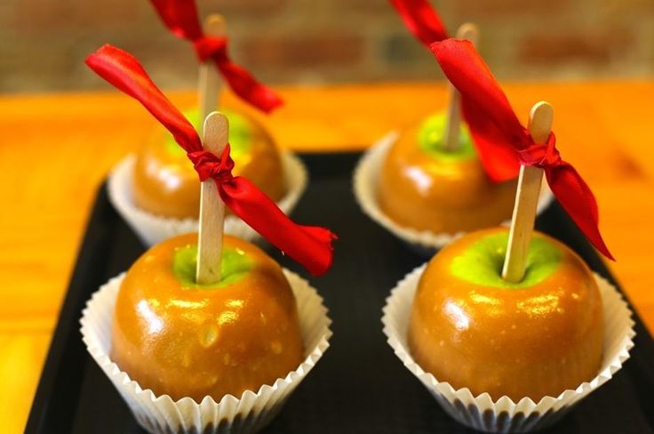 three caramel apples with toothpicks in them sitting on a black platter