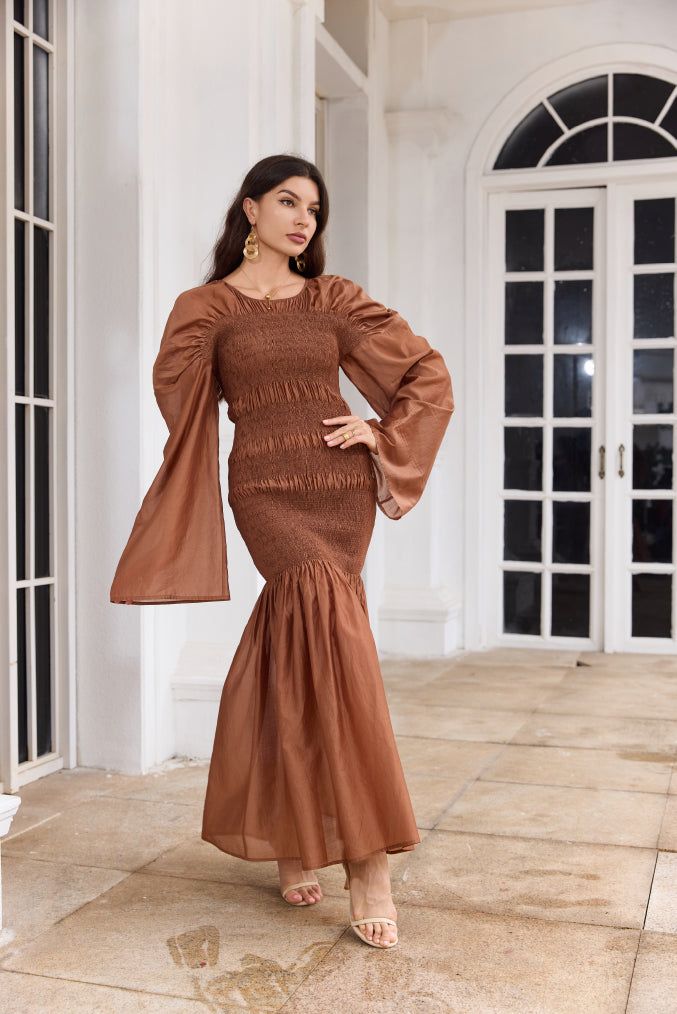 Introducing the Sienna Gown from Leah Anthoni, a stunning homage to the earth's natural beauty and the warmth of an autumn sunset. This gown is designed for the woman who carries the essence of elegance and grace in her every step. Crafted in luxurious, warm brown fabric, the Sienna Gown envelops you in comfort while exuding a sophisticated allure. The gown's unique texture and gentle flow pay tribute to the timeless beauty of the earth's layers, while its fitted bodice and flared skirt create a Fall Evening Maxi Dress With Gathered Sleeves, Evening Maxi Dress With Elastic Sleeves For Fall, Fall Evening Maxi Dress With Elastic Sleeves, Fall Maxi Dress With Gathered Sleeves, Fall Maxi Dress With Gathered Sleeves And Fitted Bodice, Fall Gathered Sleeves Fitted Maxi Dress, Fall Fitted Maxi Dress With Gathered Sleeves, Fall Maxi Dress With Gathered Sleeves And Fitted Design, Elegant Fall Maxi Dress With Elastic Sleeves