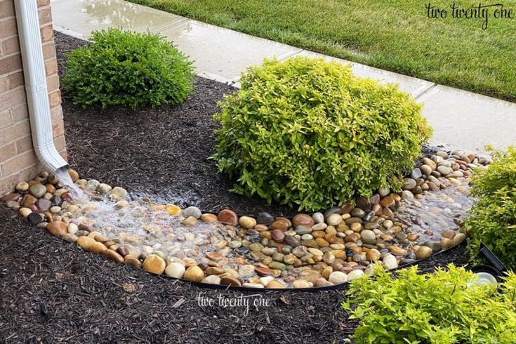 a garden with rocks and water flowing from the top to bottom, in front of a house