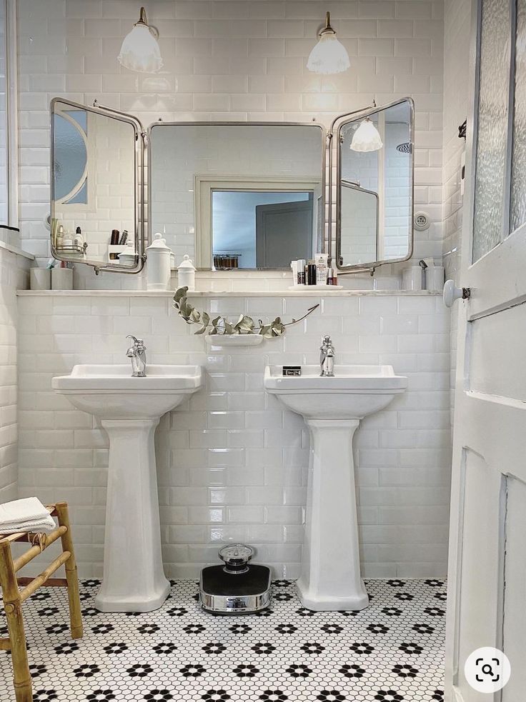 a white bathroom with black and white tile flooring, two pedestal sinks and a mirror on the wall