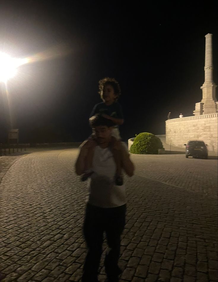 a man holding a young boy on his shoulders in front of a monument at night