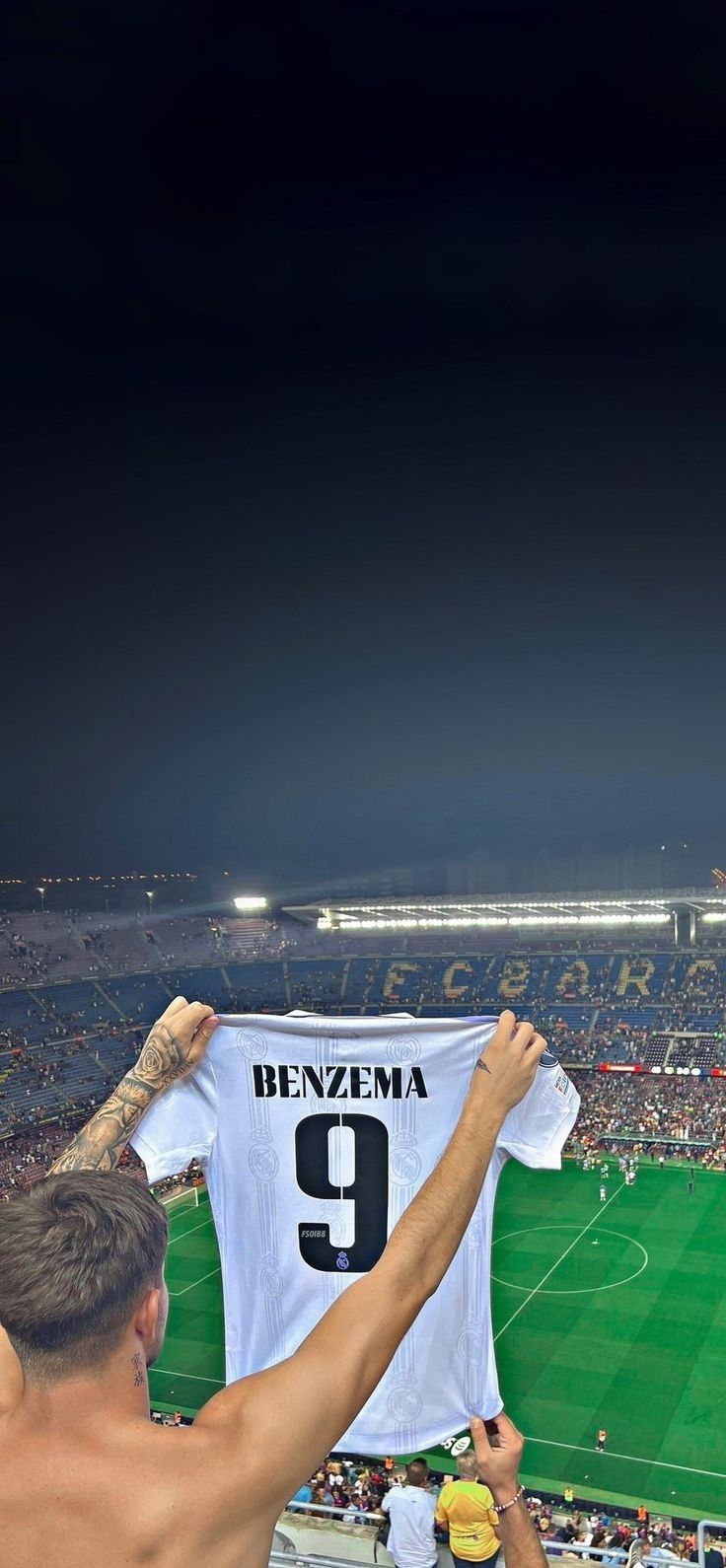 a man holding up a soccer jersey in front of a stadium full of people at night