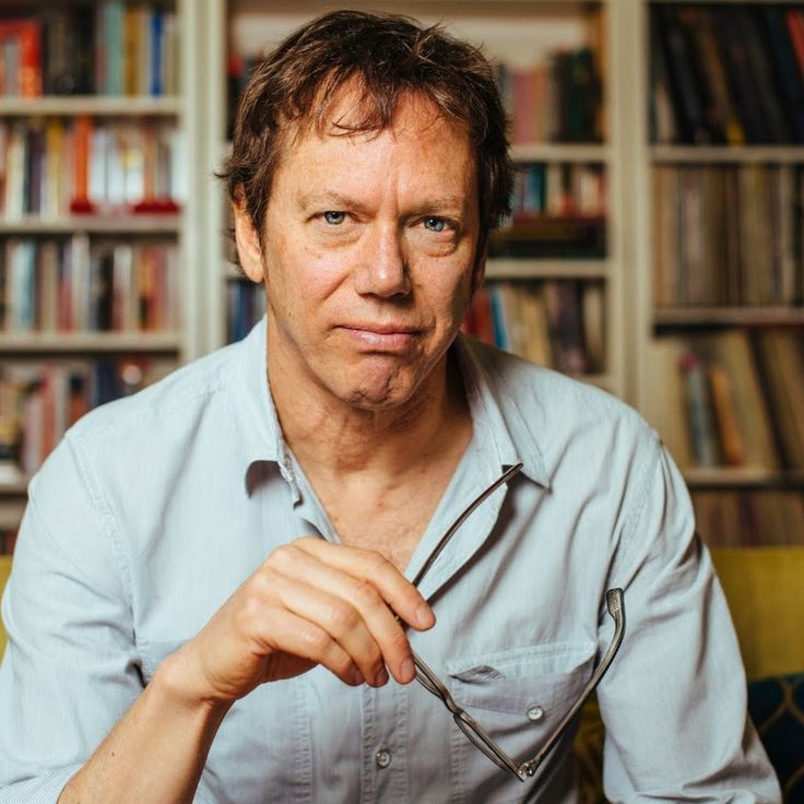 a man is holding a fork and looking at the camera while sitting in front of bookshelves